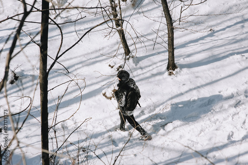 An adult man, a wanderer, a tourist in black clothes with a backpack on his back walks through the snowy forest in winter, enjoying the beautiful nature and fresh air. Photography, concept.