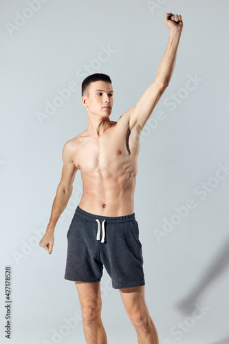 sport man in shorts doing exercise leaning forward on gray background cropped view