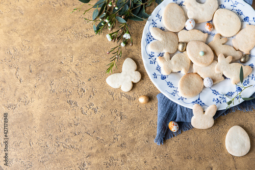 Easter cookies on a ceramic plate with floral decor and candies shaped eggs, stone background. Homemade butter and sugar cookies. Holiday concept. Top view. Copy space. photo