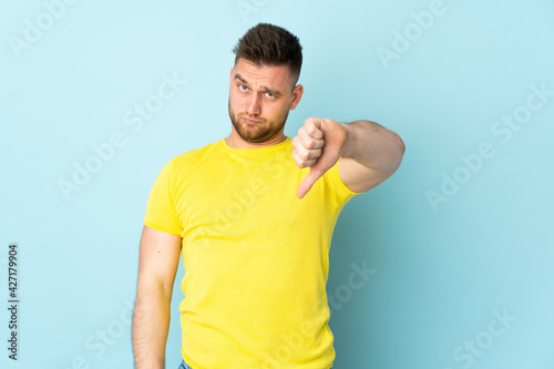 Russian handsome man isolated on blue background showing thumb down with negative expression