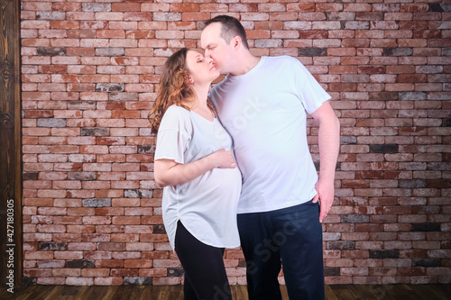 An adult married couple a man and a woman in casual clothes kiss against the background of a red brick wall