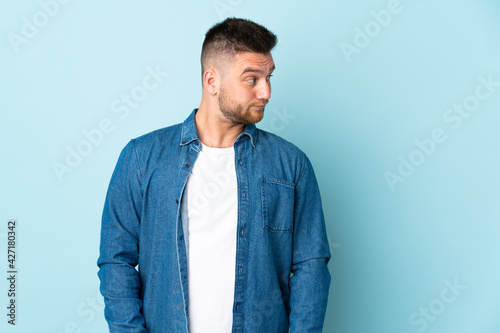 Russian handsome man isolated on blue background making doubts gesture looking side