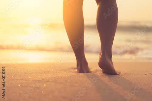 Close up woman legs walking on tropical sunset beach with smooth wave and bokeh sun light wave abstract background. Travel vacation and freedom feel good concept.