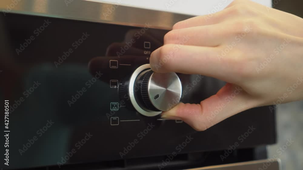 A woman's hand adjusting the electric oven in the kitchen, close-up. It turns the wheel and sets the mode and temperature. A woman's hand adjusting the electric oven in the kitchen, close-up. It turns the wheel and sets the mode and temperature.