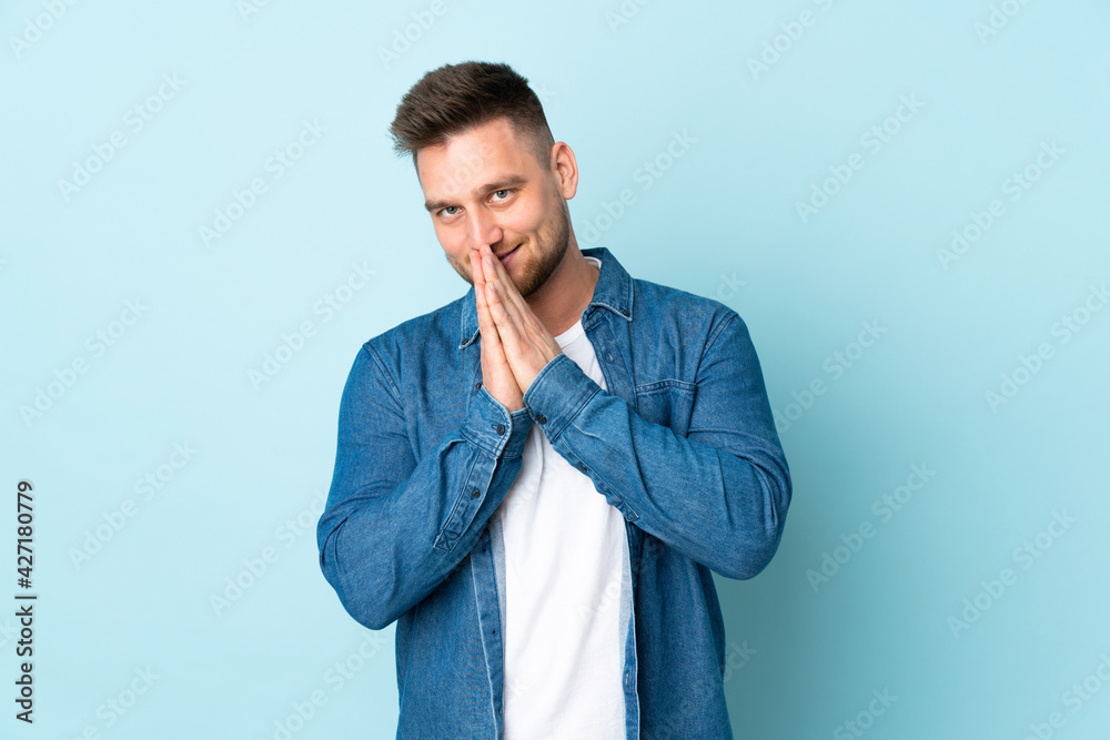 Russian handsome man isolated on blue background keeps palm together. Person asks for something