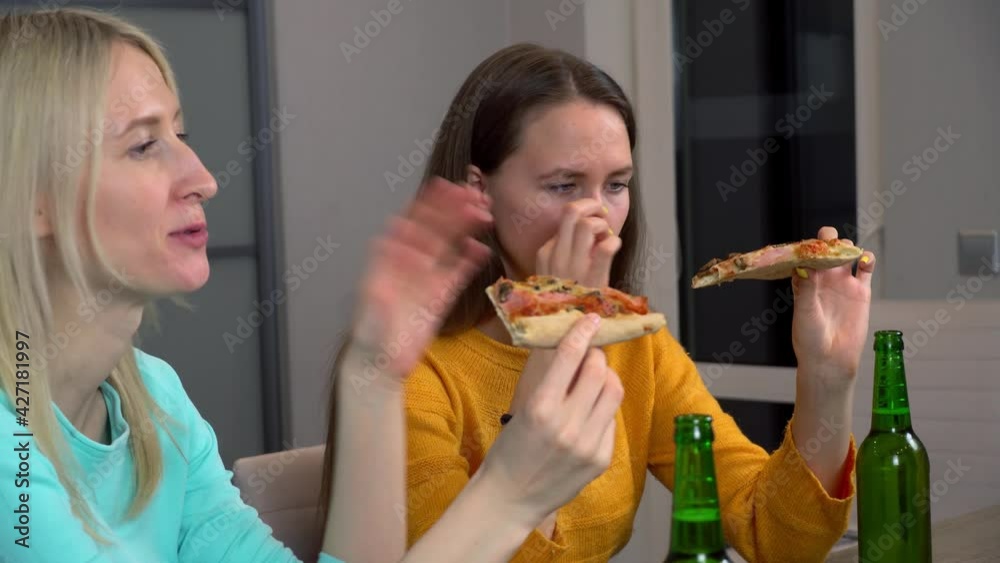 Relax with your friend. Two best happy girlfriends at home in the kitchen eating pizza and drinking beer. They laugh and smile. celebrating. Relax with your friend. Two best happy girlfriends at home in the kitchen eating pizza and drinking beer. They laugh and smile. celebrating.