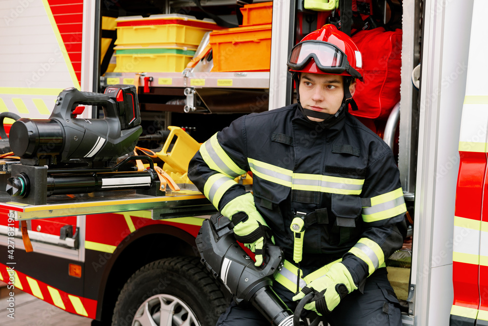 A man of strong physique in uniform and helmet stands by a rescue vehicle. A man of strong physique in uniform and helmet stands by a rescue vehicle.
