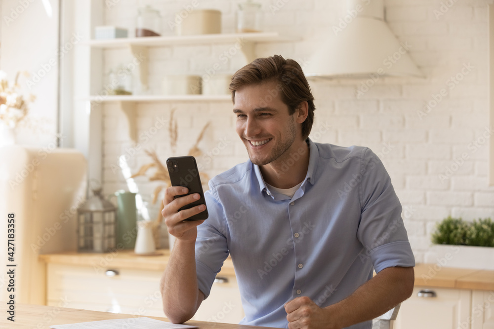 Close up overjoyed man looking at phone screen, having fun with mobile device, excited young male browsing apps, enjoying leisure time, chatting or shopping online, sitting at table in kitchen Close up overjoyed man looking at phone screen, having fun with mobile device, excited young male browsing apps, enjoying leisure time, chatting or shopping online, sitting at table in kitchen