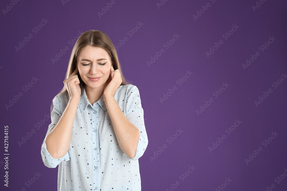 Emotional young woman covering her ears with fingers on purple background. Space for text Emotional young woman covering her ears with fingers on purple background. Space for text