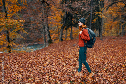 happy travel woman with backpack walks through the autumn park in nature near the river landscape tall trees sweater © SHOTPRIME STUDIO