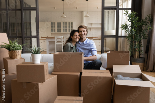 Portrait happy family sitting on couch with cardboard boxes, relocation and moving day concept, smiling wife and husband looking at camera, preparing to relocation, mortgage or rent concept © fizkes