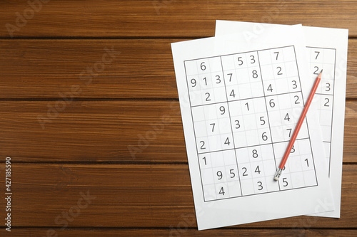 Sudoku and pencil on wooden table, top view. Space for text