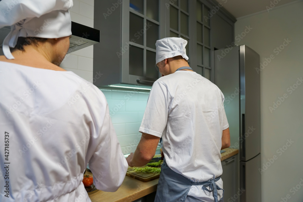 Two chefs in the restaurant kitchen prepare dinner. The chef is dressed in a white tunic and a chef's hat.