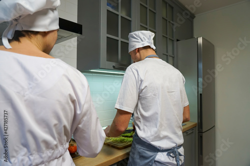 Two chefs in the restaurant kitchen prepare dinner. The chef is dressed in a white tunic and a chef's hat.