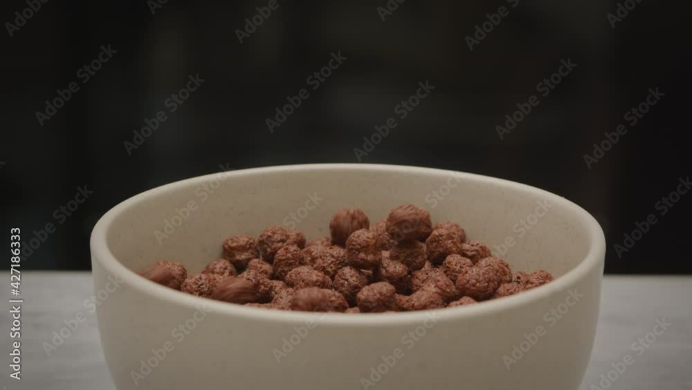 Close up macro shot of chocolate corn flakes pouring into a bowl plate on a dark background Close up macro shot of chocolate corn flakes pouring into a bowl plate on a dark background