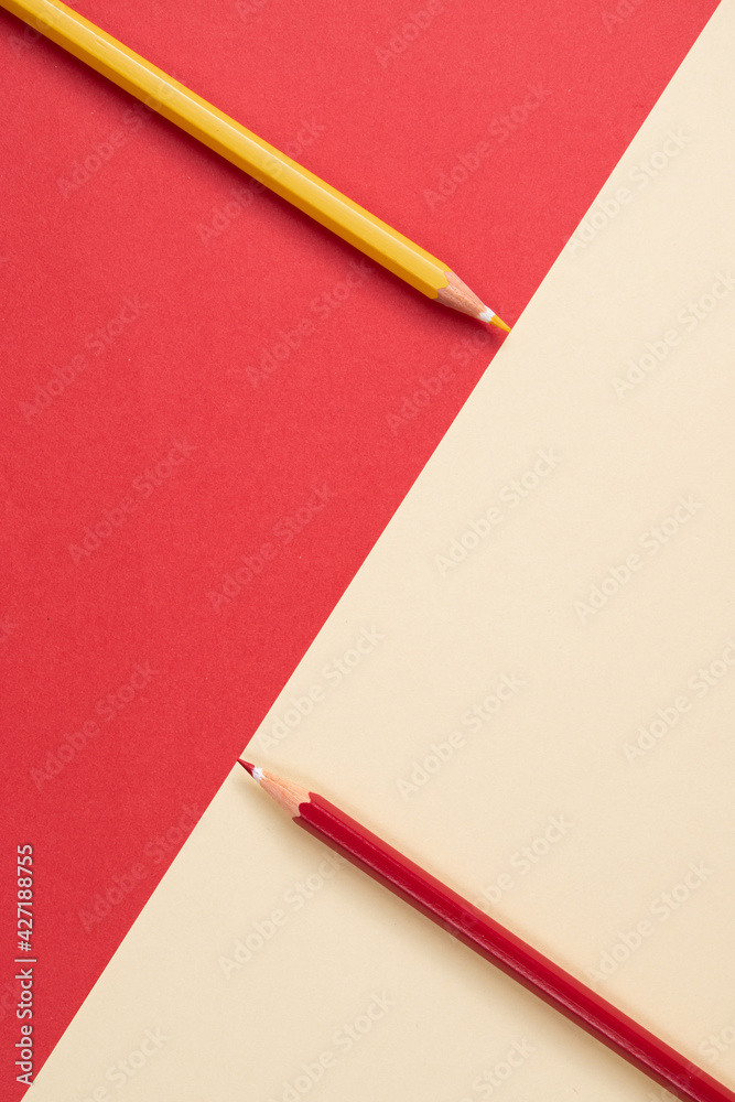 top view. colored pencils touching the division of the image which is a diagonal line dividing the area into two backgrounds of red and beige. yellow and red pencils. top view. colored pencils touching the division of the image which is a diagonal line dividing the area into two backgrounds of red and beige. yellow and red pencils.