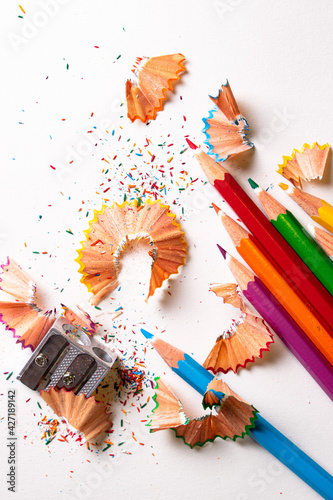 Top view of colored pencils with shavings and pencil sharpener over white background. top view.