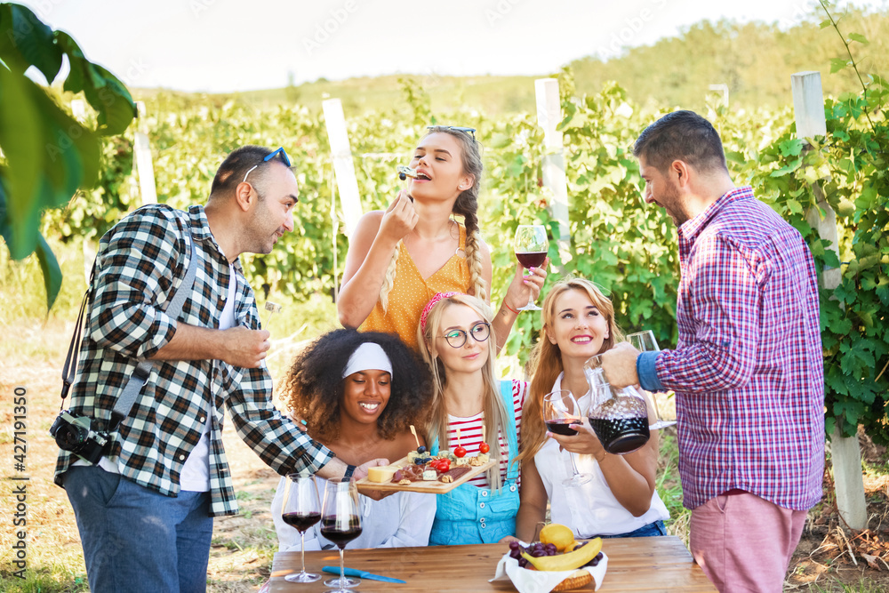 Happy friends having fun tasting red wine in vineyard