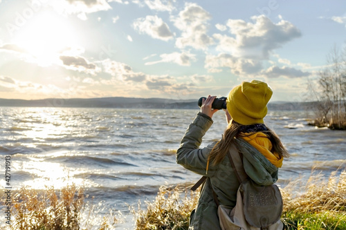 Young woman looking through binoculars at birds on the lake. Birdwatching, zoology, ecology. Research in nature, observation of animals. Ornithology photo