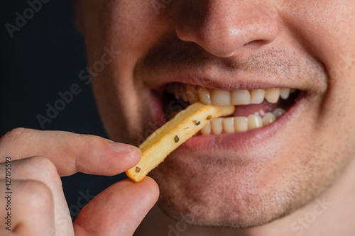 Young man bites fries. Extreme close up. Guy eats eating fried potatoes, isolated. Male mouth.