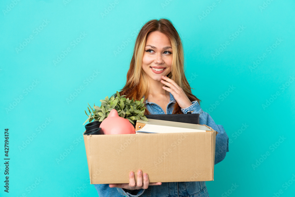 Teenager blonde girl making a move while picking up a box full of things looking to the side and smiling Teenager blonde girl making a move while picking up a box full of things looking to the side and smiling