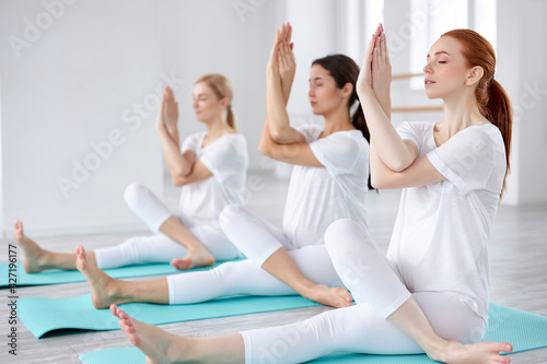 three attractive diverse ladies sit on fitness mat doing yoga exercises