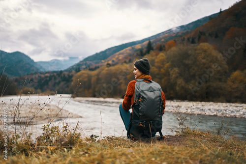 woman with backpack on the river bank admires the mountain landscape in the background © SHOTPRIME STUDIO