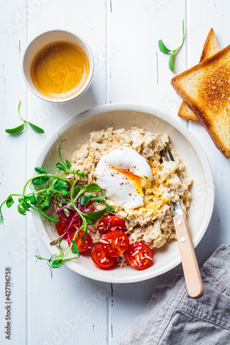 Savory oatmeal with poached egg, tomatoes, cheese and sprouts in white bowl, top view. Healthy breakfast concept.