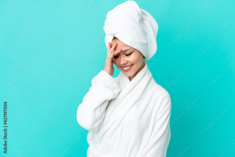 Teenager blonde girl in a bathrobe over isolated blue background laughing Teenager blonde girl in a bathrobe over isolated blue background laughing
