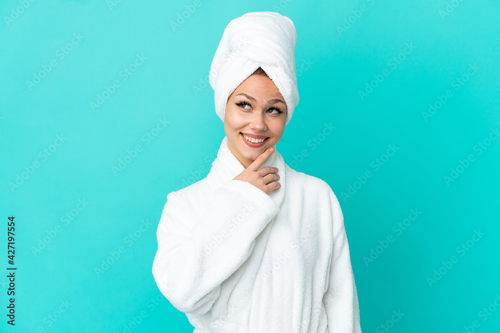 Teenager blonde girl in a bathrobe over isolated blue background looking up while smiling Teenager blonde girl in a bathrobe over isolated blue background looking up while smiling