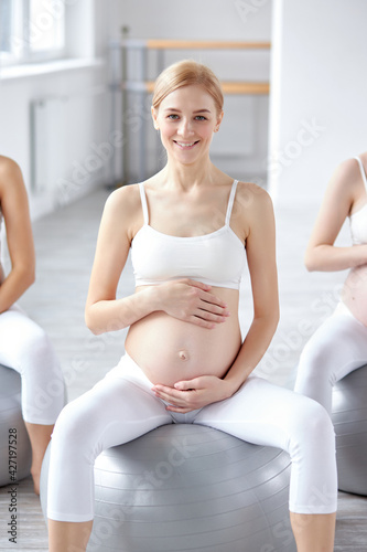 happy blonde pregnant woman sit on fitball hugging tummy