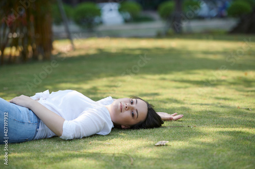 Attractive young brunette relaxing on green grass in city park and smiing at camera © DragonImages