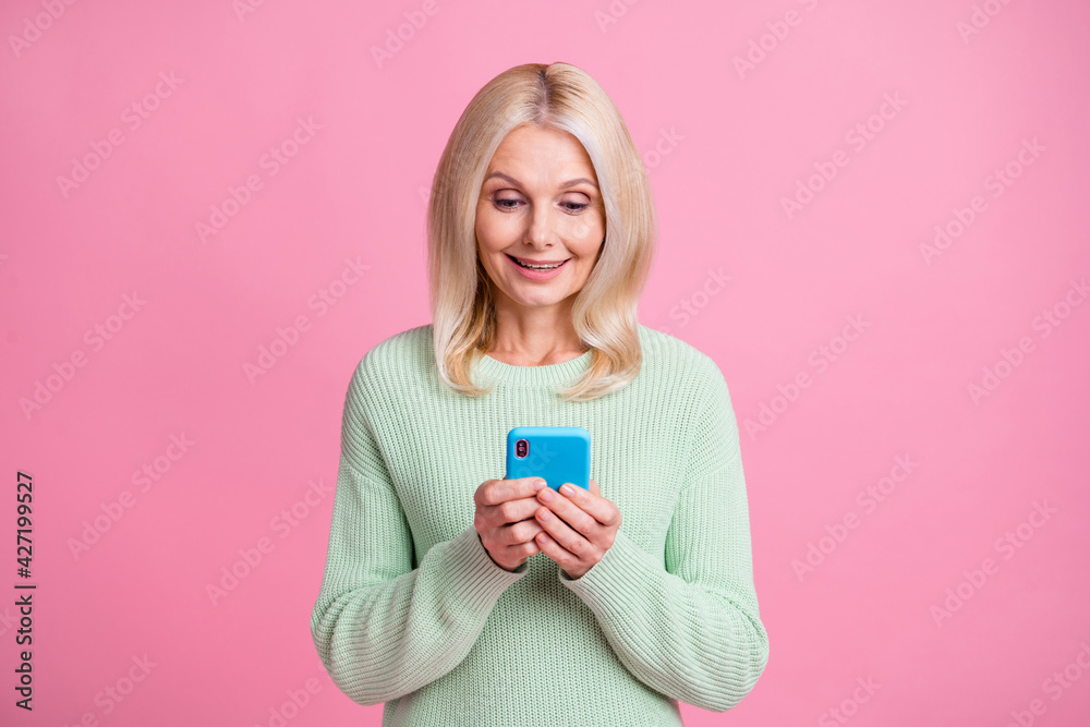 Photo portrait of smiling elderly woman browsing holding phone in two hands isolated on pastel pink colored background Photo portrait of smiling elderly woman browsing holding phone in two hands isolated on pastel pink colored background