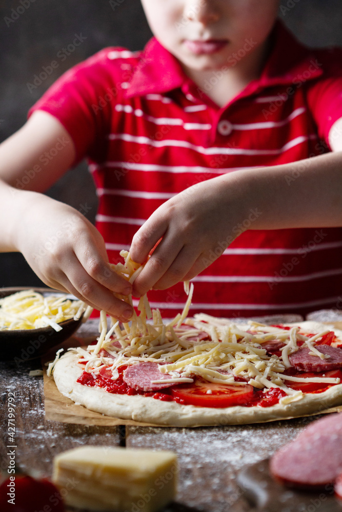 Child prepares pizza, lays out grated cheese