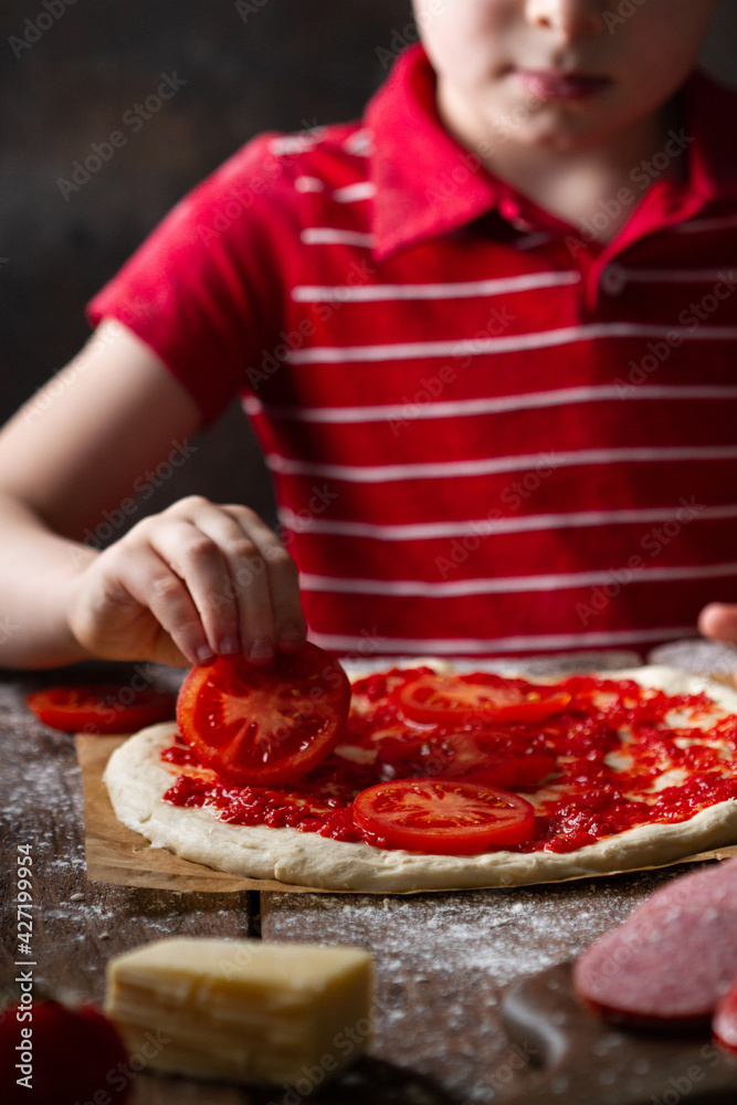 Child's hand lays tomato slices on future pizza