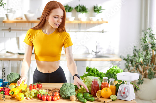 pretty nice woman with lots of healthy fresh food in kitchen. Concept of losing weight, sports and healthy eating
