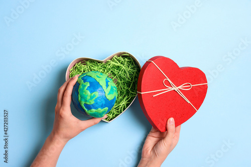 Fototapeta Naklejka Na Ścianę i Meble -  Female hands holding heart gift box with planet earth on a blue background. Earth Day.