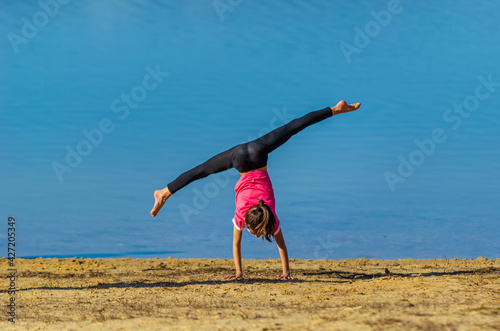 7 years old girl with pink shirt and sportswear doing a cartwheel at the beach during spring with blue water as background. Palencia, Spain