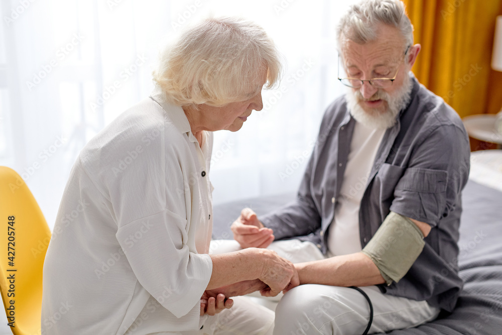 Mature woman controlling blood pressure of husband using stethoscope Mature woman controlling blood pressure of husband using stethoscope