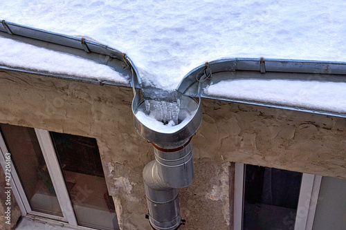 Fragment of the snow-covered roof of an old house with a drain with frozen water