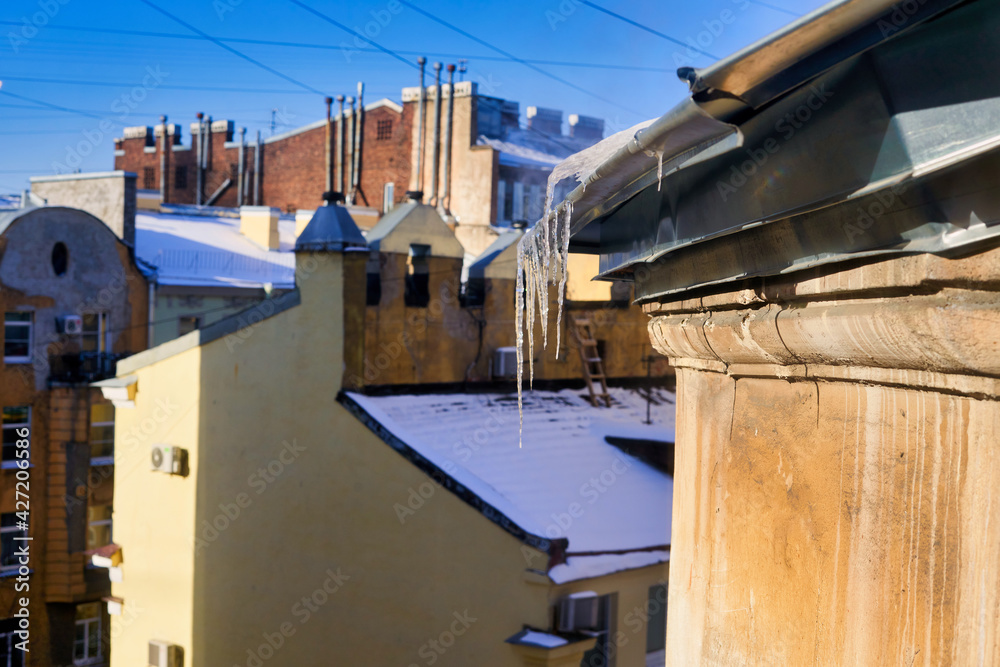 View of snow-covered roofs with spring icicles against blue sky View of snow-covered roofs with spring icicles against blue sky
