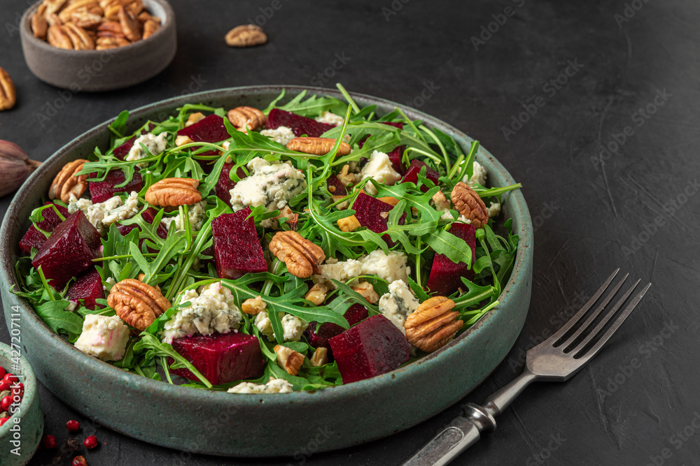 Arugula, beet and blue cheese salad with pecan nuts in a plate with fork on black table background. healthy vegetarian food
