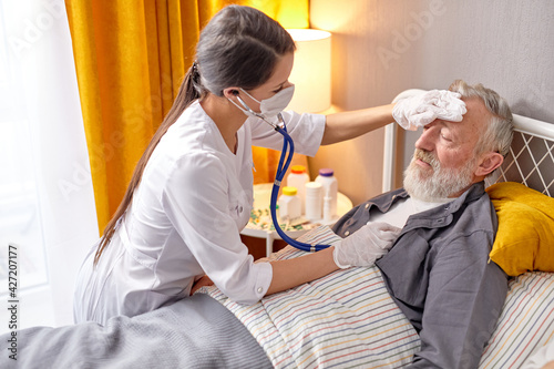 Bilde på lerret Young nurse take care senior man on a bed, nurse listen to sounds in heart or lu