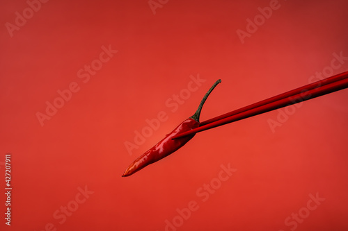 Red Chinese chopsticks derazht a small red hot chili pepper. Red on red. Ingredients for Asian food. Spicy food. Red background. Asian products. Macro photography of food. © Margarita Kaprize