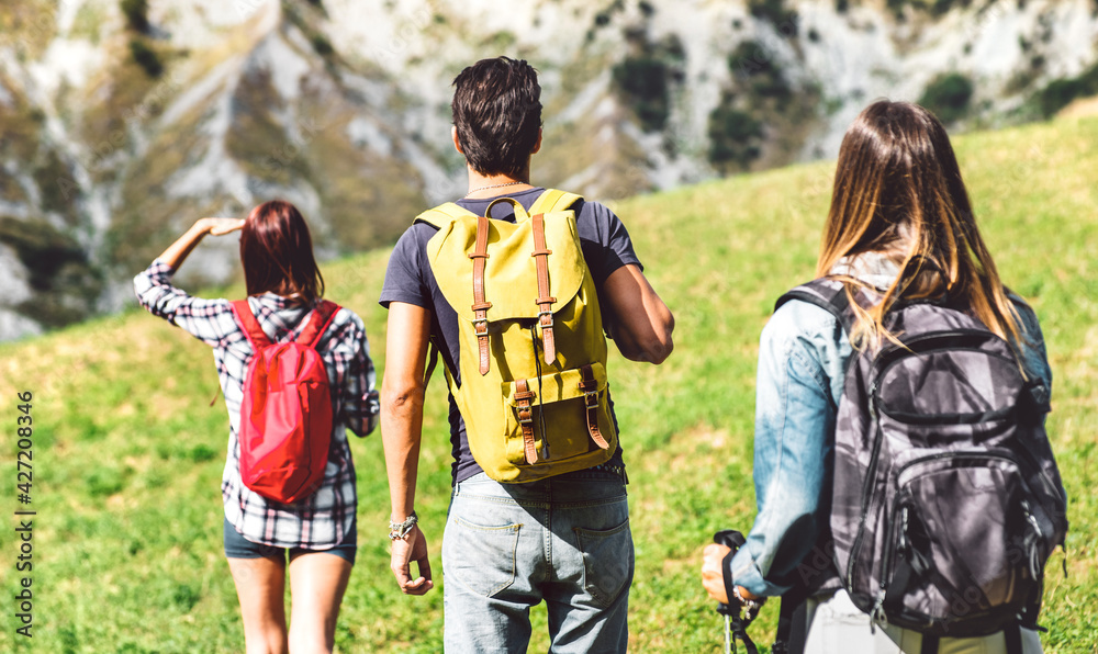 Friends group trekking on italian alps at afternoon - Hikers walking on mountain place - Wanderlust travel concept with young people at excursion in wild nature - Focus on central yellow backpack