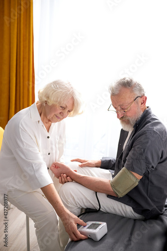 Woman controlling blood pressure of husband with tonometer, side view