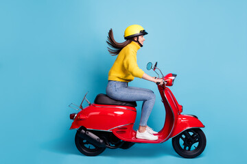 Full length side profile photo portrait of woman riding red scooter isolated on pastel blue colored background