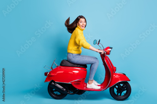 Full size profile photo of astonished pretty lady driving moped open mouth smile isolated on blue color background © deagreez