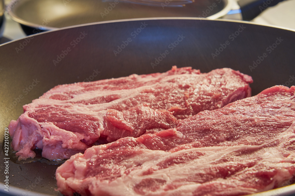 Salted red pork steaks in a frying pan.