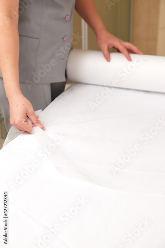 Woman massage therapist spreading disposable sheet on massage table